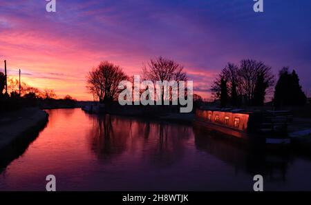 Le soleil brûlant rouge jette une lueur orange sur un bateau étroit amarré sous un ciel bleu glacé et froid sur le canal de Leeds et Liverpool près de Burscough Banque D'Images