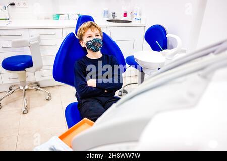 L'enfant avec un masque anticosvid attend dans une chaise de dentiste pour être traité. Banque D'Images