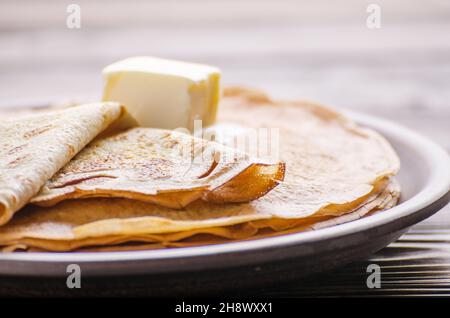 Pile de crêpes françaises avec le beurre dans un plat en céramique sur une table de cuisine en bois Banque D'Images