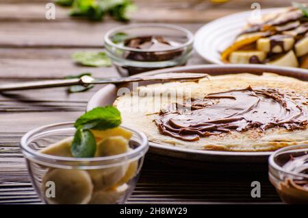 Crêpes français avec une sauce au chocolat et de la banane dans la cuvette d'argile sur la table de cuisine en bois Banque D'Images