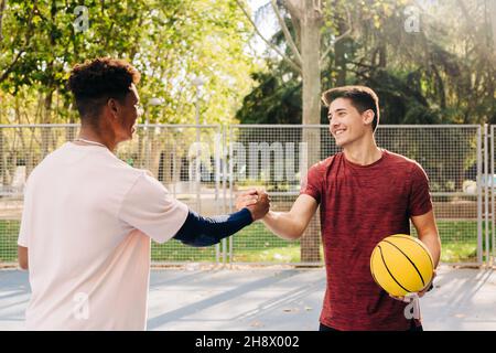 Jeunes athlètes masculins avec des mains de basket-ball jaunes tout en se tenant debout sur le terrain de sport dans le parc Banque D'Images