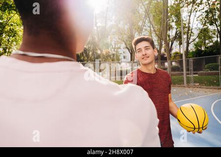 Jeunes athlètes masculins avec des mains de basket-ball jaunes tout en se tenant debout sur le terrain de sport dans le parc Banque D'Images