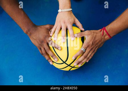 De dessus de crop anonyme joueurs masculins mettant les mains sur le ballon jaune de basket-ball sur la surface bleue de sportsground Banque D'Images