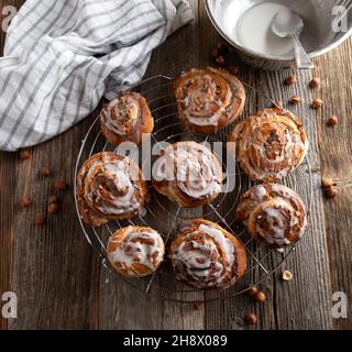 Petits pains à la cannelle faits maison avec garniture noisette sur une grille de refroidissement sur une table en bois Banque D'Images