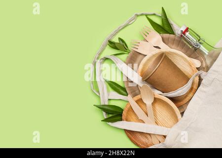 Tasse jetable, assiettes et couverts en bois dans un sac textile sur fond vert Banque D'Images