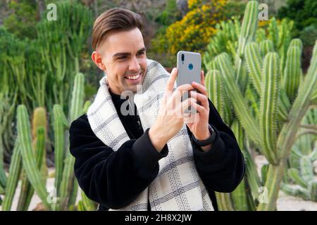 Jeune homme élégant et sûr de lui-même dans une tenue à la mode prenant des photos dans un parc tropical Banque D'Images