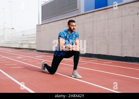 Homme sportif avec des vêtements de sport s'étendant sur la piste de course à pied Banque D'Images