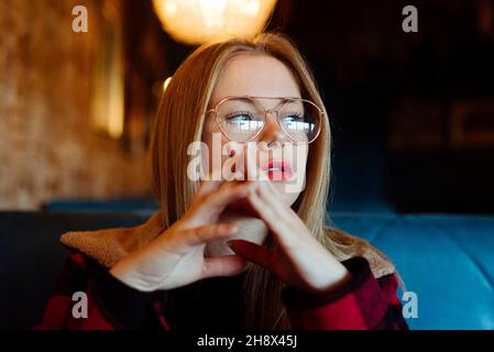 Cette jeune femme blonde pleine d'assurance est assise sur un café et regarde loin Banque D'Images