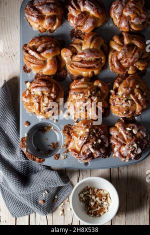 Vue de dessus pile de délicieux petits pains à la cannelle maison fraîchement cuits placés sur une table en bois avec des noix de rocade dans la cuisine légère Banque D'Images