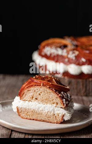 Une tranche appétissante de gâteau du roi farcie de crème blanche sur une assiette placée sur une table en bois sur fond noir Banque D'Images