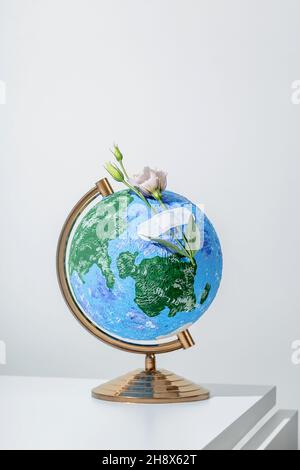 Globe of Planet Earth avec des fleurs attachées avec un bracelet médical placé sur une surface blanche Banque D'Images