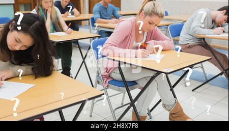 Image numérique composite des étudiants de l'université qui écrivent des examens sur des bureaux en classe avec des points d'interrogation Banque D'Images