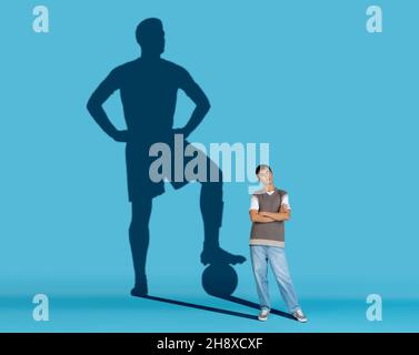 Homme rêvant d'un grand et célèbre avenir sportif.Image conceptuelle avec garçon et ombre du joueur de football sur fond bleu Banque D'Images