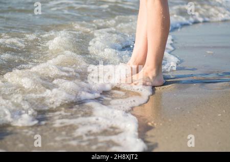 Les jambes des femmes sont couvertes par la vague de mer. Les pieds dans l'eau en gros plan. Banque D'Images