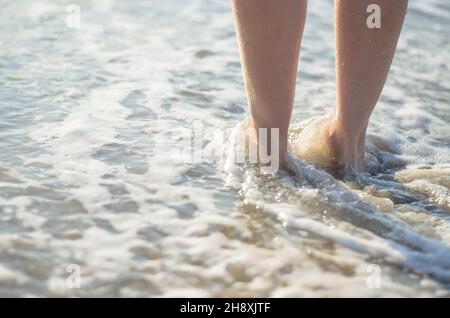 Les jambes des femmes sont couvertes par la vague de mer. Les pieds dans l'eau en gros plan. Banque D'Images