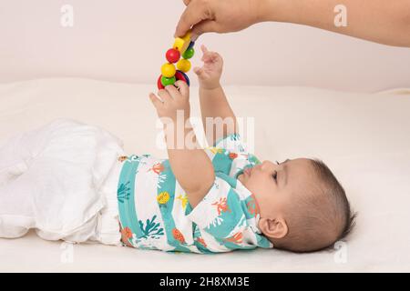 bébé garçon de 3 mois dans le dos pour atteindre le jouet adulte est pendant au-dessus de lui Banque D'Images