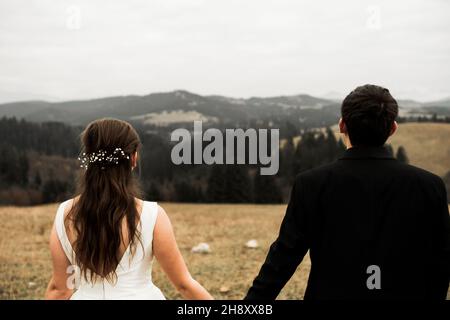 La mariée et le marié tiennent les mains et regardent vers l'avenir au milieu de la nature, les jeunes mariés marchent ensemble, photographie de mariage, jusqu'à ce que la mort nous fasse partie Banque D'Images