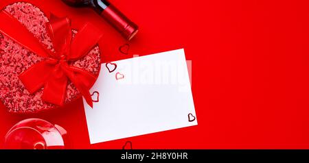 Vin, verres et boîte cadeau en forme de coeur avec un ruban rouge sur fond de scarlet. Carte postale concept de la Saint-Valentin. Vue de dessus. Plan d'étapage avec vue de dessus Banque D'Images