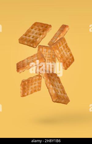 Gaufres douces volantes dans l'air, isolées sur fond jaune.Concept alimentaire créatif. Banque D'Images
