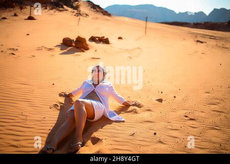 une touriste femelle s'est assise pour se reposer dans le désert sur le sable et regarde le ciel Banque D'Images