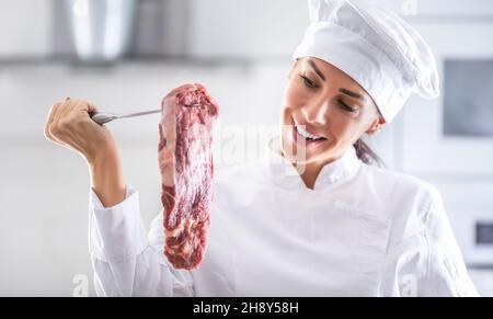 Le chef féminin de rondon lève un steak de bœuf rouge qui lui donne l'air d'être souriant. Banque D'Images