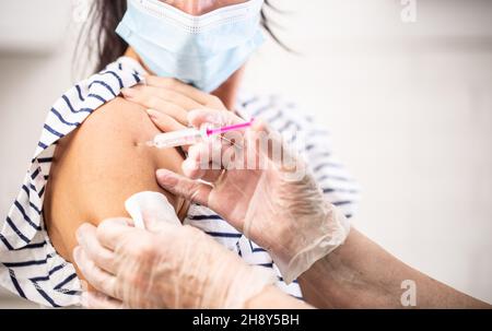Détail du médecin mettant le vaccin Covid-19 par injection dans le bras d'une femme portant un masque facial. Banque D'Images