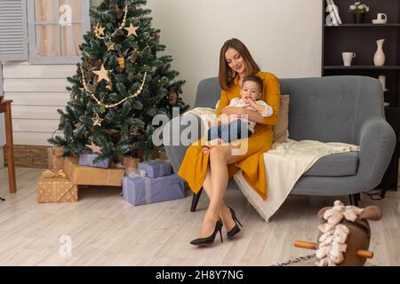 Belle femme mince en robe assis avec un bébé dans un salon Banque D'Images