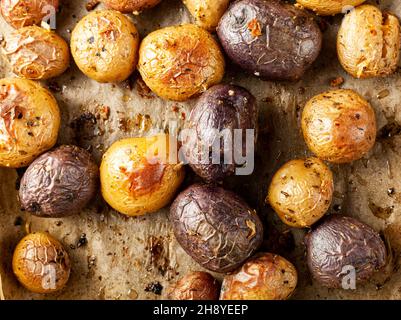 Vue de dessus gros plan montrant la médley de pommes de terre fraîche cuite au four avec une variété comprenant des pommes de terre au coeur pourpre.Les pommes de terre refroidissent sur du papier de cuisson.C Banque D'Images