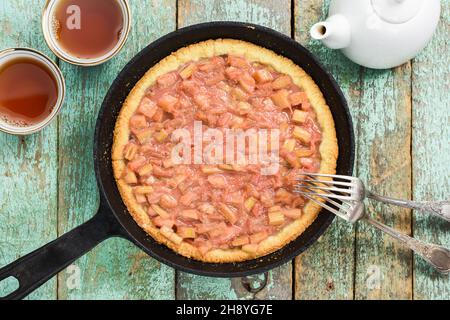 Tarte à la rhubarbe maison délicieuse dans une poêle en fonte sur des planches turquoise avec vue sur le thé noir Banque D'Images