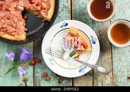 Tarte à la rhubarbe maison avec fraises forestières fraîches sur de vieux tableaux turquoise avec thé et fleurs de bellflower Banque D'Images