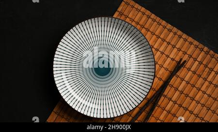 Table avec plaque en céramique bleue et blanche avec baguette sur placaret en bambou dans table sombre. Vue du dessus, plat Banque D'Images