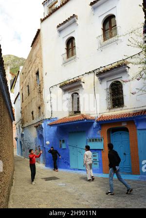 Des garçons marocains jouant au football entre les maisons peintes traditionnellement en bleu dans la médina de Chefchaouen, dans les montagnes de Rif, dans le nord du Maroc. Banque D'Images