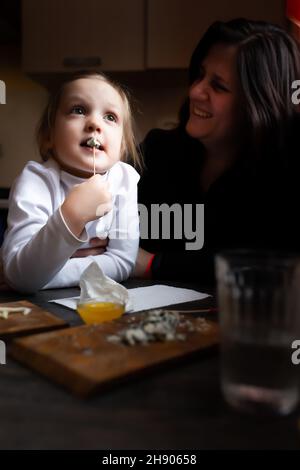 Une fille mange du fromage avec de la moisissure bleue dans les bras de sa mère dans une maison de campagne. Banque D'Images