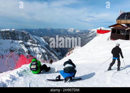 Au sommet de la piste de ski, les snowboarders s'enfilent sur leurs planches et les skieurs se mettent en route.En arrière-plan sont les chaînes de montagnes, le ciel bleu et le nuage Banque D'Images