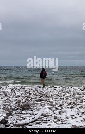 Un homme debout sur une plage rocheuse couverte de neige et de vagues s'écrasant Banque D'Images