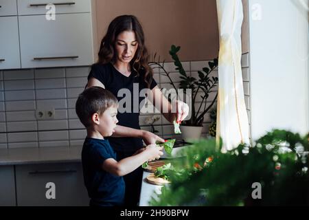 mère et fils préparent des légumes frais pour la salade au déjeuner dans la cuisine Banque D'Images