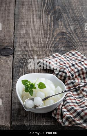 Petits oignons marinés dans une soucoupe blanche sur une table en bois Banque D'Images