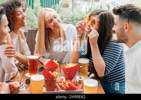 Des amis multiraciaux gaies dans des vêtements décontractés s'amuser tout en étant assis à table avec des verres de bière et de savoureux en-cas sur la terrasse dans le café en journée Banque D'Images