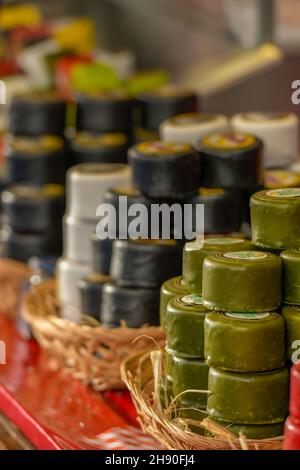 sélection de fromages cirés dans des emballages rouges verts et noirs sur une cabine dans un marché festif de noël, fromages ronds à vendre sur une étalle de marché, chesses Banque D'Images