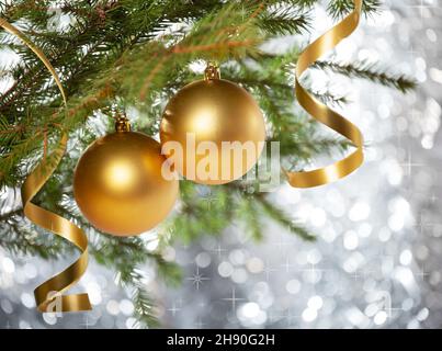 Décorations de Noël.Deux boules d'or et boucles en serpentin sur une branche d'un arbre de noël, sur un fond de bokeh argenté avec des sparkles Banque D'Images