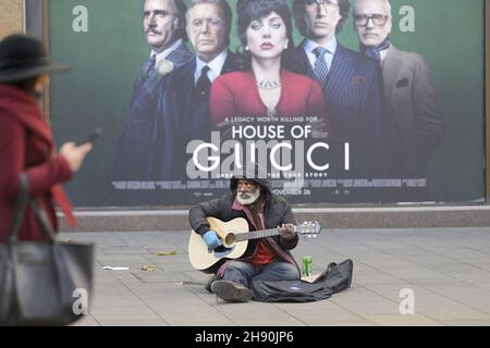 Londres, Angleterre, Royaume-Uni.Vieil homme noir en bus/mendiant à Leicester Square devant une affiche pour House of Gucci - décembre 2021 Banque D'Images