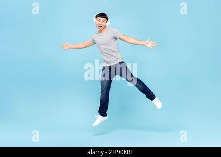 Jeune homme asiatique énergique, portant un casque, écoutant de la musique et sautant sur fond bleu clair isolé Banque D'Images