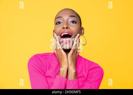 Gros plan portrait d'une jeune femme afro-américaine surprise avec les mains sur les joues isolées sur fond jaune studio Banque D'Images