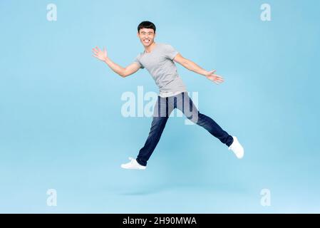 Tir de saut de jeune asiatique éstatique avec des bras levant dans l'air moyen isolé dans un fond bleu studio Banque D'Images