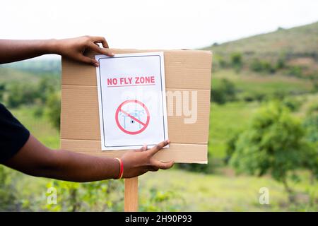 Gros plan des mains collant panneau de zone d'interdiction de vol à bord à drone zone restreinte comme règlement de sécurité - concept de zone restreinte de drone. Banque D'Images