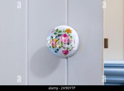 Gros plan sur une porte ronde en porcelaine de style victorien décorée de fleurs bouton sur une porte de style grange en bois blanc. Banque D'Images