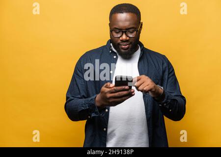 Photo d'homme noir barbu attrayant dans une chemise décontractée avec smartphone isolé sur fond gris, touche l'écran du téléphone, outil nécessaire pour la productivité, trouve l'inspiration en ligne Banque D'Images