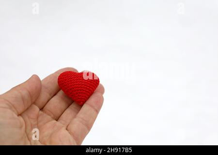 Coeur tricoté rouge dans la paume de la main mâle contre la neige.Concept d'amour d'hiver, de Saint-Valentin ou de charité Banque D'Images