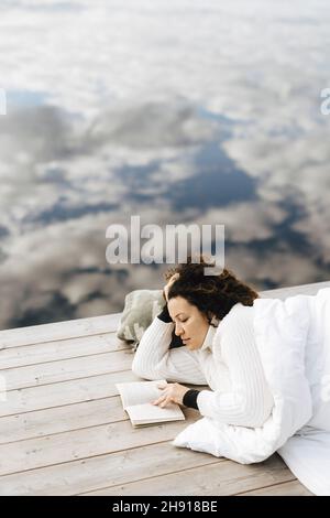 Jeune femme lisant le livre en étant couché sur la jetée Banque D'Images