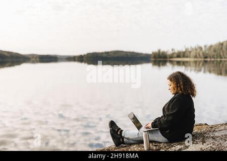 Femme travaillant sur un ordinateur portable à distance au bord du lac pendant le week-end Banque D'Images